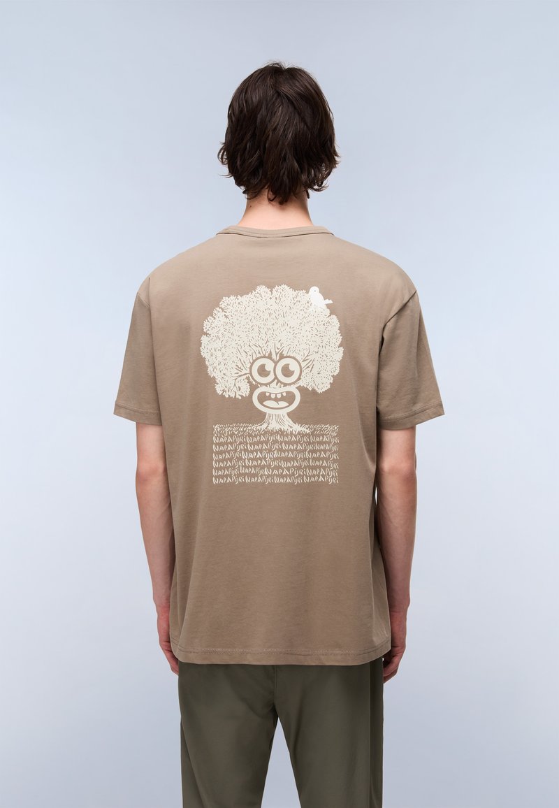 Brązowa koszulka bawełniana z dużą grafiką drzewa z twarzą i ptakiem, nadrukowana w kremowym kolorze na plecach. Krótkie rękawy i okrągły dekolt.