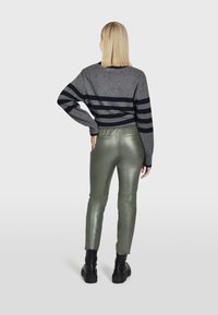 Grijze gestreepte trui met marineblauwe en donkergrijze strepen, gecombineerd met glanzende olijfgroene strakke broeken en zwarte chunky laarzen.