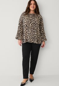 Bluse med leopardmønster i blødt stof med lange, udvidede ærmer, parret med sorte tætsiddende bukser og spidse sorte hæle.