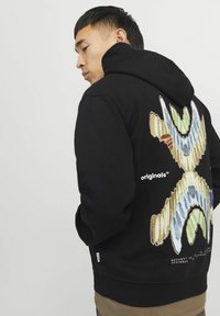 Sort hætte sweatshirt med et farverigt abstrakt design på ryggen. Har en rummelig hætte og ribbede manchetter. Stof ser blødt og struktureret ud.