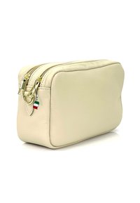 Crème leren cosmeticatas met een rechthoekige vorm, dubbele ritsen, gouden hardware en een klein Italiaans vlaggetje als hanger.