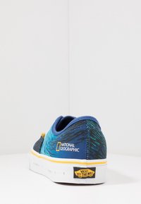 Sneaker Vans blu e teal con fantasia, caratterizzati da una suola bianca, dettagli gialli e il logo del National Geographic sul lato.