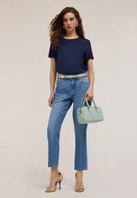 Top corto navy a maniche corte, jeans a vita alta blu chiaro, borsa verde menta e tacchi alti gialli con cinturini. Dettaglio della cintura dorata.