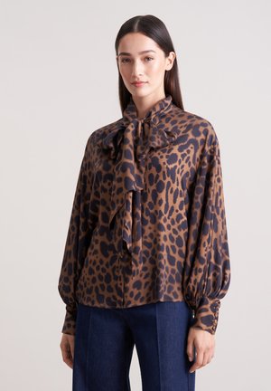 Blusa in misto seta con stampa leopardata, caratterizzata da un collo con fiocco, maniche lunghe ampie e una texture liscia. Toni di marrone e blu scuro.