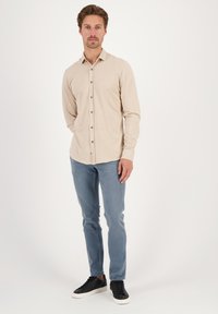 Camisa de botones de manga larga en color beige claro con una textura sutil, combinada con jeans ajustados de color azul claro y zapatillas negras con cordones.
