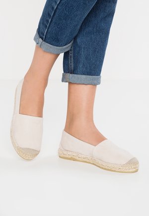 Lyse beige espadriller med en glat ruskindsoverdel, jutevævet mellemsål og rund tå. Rullede denimjeans er opsmøgede over anklen.