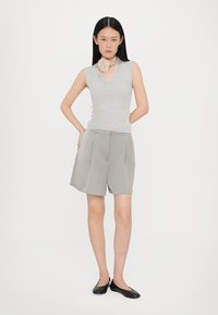 Top grigio senza maniche con scollatura a V e sottile trama a coste, abbinato a pantaloni corti grigi chiari con pieghe. Gli accessori includono un colletto testurizzato.