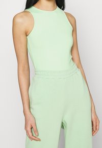 Bodysuit sans manches vert clair avec un col montant, fabriqué dans un tissu lisse, complété par un pantalon taille haute assorti avec une taille élastique.