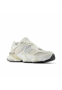 Białe i beżowe sneakersy New Balance z meshowymi i zamszowymi panelami, grubą podeszwą oraz czarnymi akcentami na podeszwie i logo.