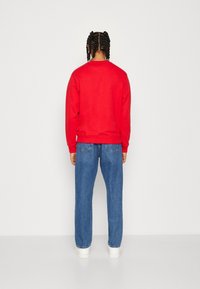 Sudadera de algodón roja con cuello redondo, combinada con vaqueros de mezclilla azules. Corte casual, diseño liso, y zapatillas blancas completan el conjunto.