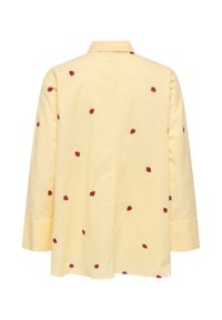 Chemise jaune clair à manches longues avec col, décorée de petits motifs de fraises rouges dispersés sur le dos et les manches.