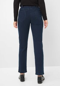 Donkerblauwe denim jeans met een rechte pijp, voorzien van twee achterzakken en een middelhoge tailleband, gecombineerd met zwarte schoenen.