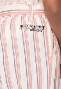 Gestreifter Stoff mit unterschiedlichen Breiten in Rosa, Orange, Grau und Weiß. Verfügt über ein schwarzes gesticktes Logo in der Nähe des Bundes.