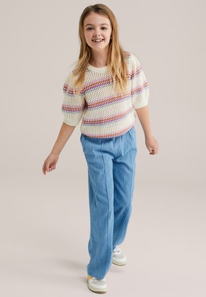 Gestrickter Pullover in lockerer Passform mit weißen, roten und lila Streifen. Kombiniert mit hellblauen, weit geschnittenen Hosen und weißen Sneakern.