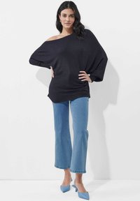 Übergroßer schwarzer gerippter Pullover mit schulterfreiem Design, kombiniert mit hellblauen Schlagjeans und hellblauen spitzen Pumps.