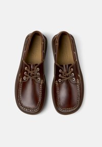 Zapatos de barco de cuero marrón con diseño de cordones, puntera redonda, costuras blancas en contraste y plantillas acolchadas, presentados desde arriba.
