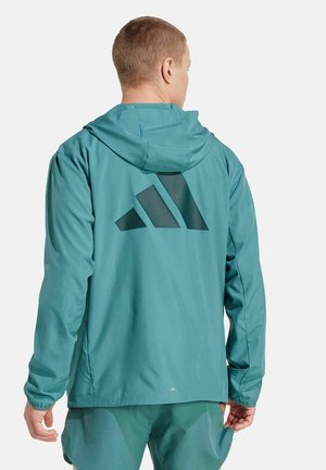 Türkise Kapuzenjacke mit glatter Textur, ausgestattet mit einem großen schwarzen geometrischen Logo auf dem Rücken und elastischen Bündchen für einen sicheren Sitz.