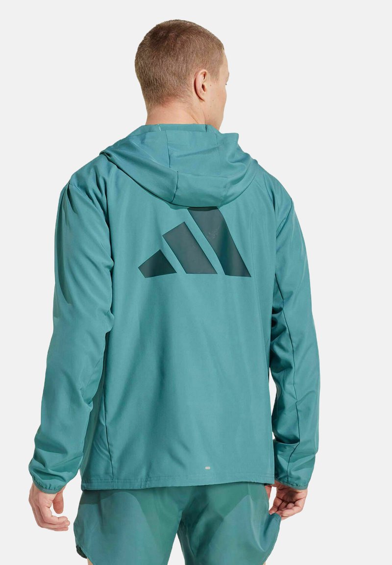 Chaqueta con capucha de color verde azulado y textura suave, con un gran logo geométrico negro en la parte posterior y puños elásticos para un ajuste seguro.