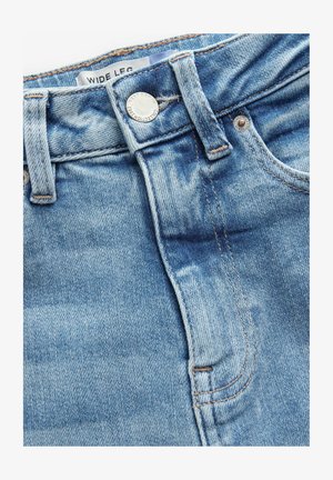 Vaqueros de mezclilla de color azul claro con patas anchas, que presentan una cintura alta, costuras visibles y una etiqueta de marca en la cintura. Cierre con botón plateado.