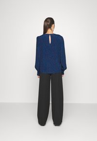 Blusa blu a motivo con maniche lunghe e dettaglio a chiave sulla schiena, abbinata a pantaloni neri larghi, con una texture di tessuto liscia.