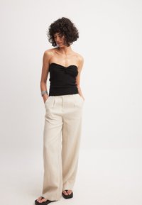 Mustmustäärne must kootud ülemine osa, millel on sõlme detail, koos beeži värvi avarate linaste pükstega. Mudel seisab käed taskutes, jalas mustad sandaalid.