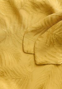 Geel stof met een bladdesign, met textured, verhoogde borduursels en een gladde zijden textuur, gevouwen om de ontwerpdetails te tonen.