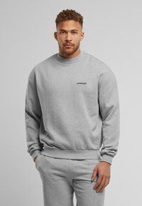 Grijze crewneck sweatshirt met ribgebreide manchetten en onderkant, met een klein zwart "UPSCALE" logo op de borst, gemaakt van zachte stof.