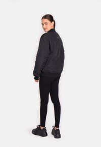 Sort bomberjakke med en glat, skinnende overflade, ribbede manchetter og kant. Sammen med sorte leggings og kraftige, sorte sneakers.