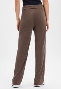 Braune Hose mit weitem Bein, weicher Strickstruktur und hohem, elastischem Bund. Mit zwei Gesäßtaschen und weiter Passform am Knöchel.