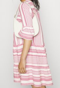 Robe blanche avec motifs roses, manches bouffantes, forme évasée à étages et texture lisse. Sac à main blanc porté à l'épaule.