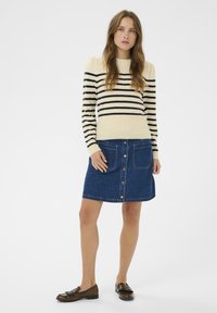 Pull rayé en ivoire et marine, associé à une jupe évasée en denim bleu avec des boutons sur le devant et deux poches latérales.