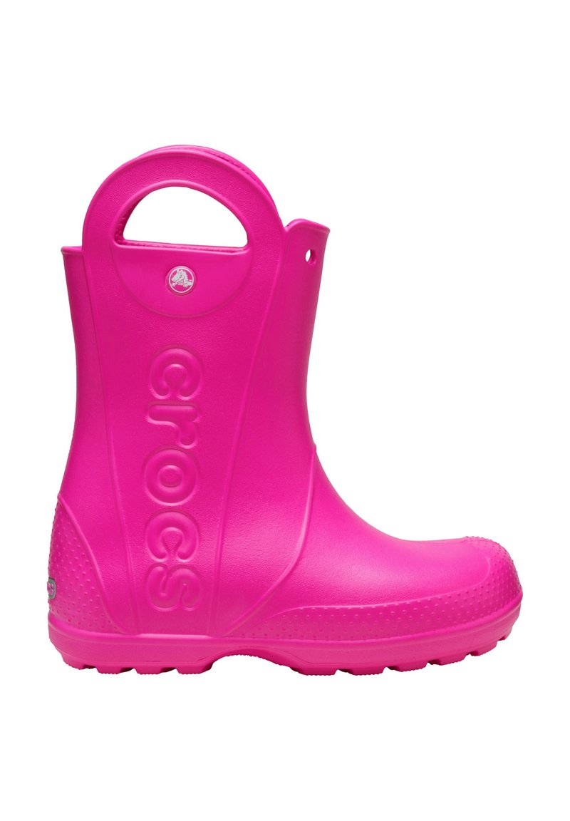 Botte de pluie en caoutchouc rose avec un bout arrondi, une semelle texturée et une poignée sur le côté. Affiche le logo "CROCS" de manière bien visible sur le côté extérieur.