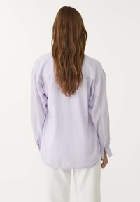 Lavendelfarbene gestreifte Hemdbluse mit langen Ärmeln und abgerundetem Saum, die einen lockeren Schnitt und eine weiche Textur aufweist.