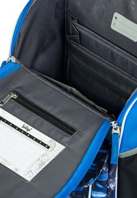 Interno di uno zaino blu con una tasca zip grigia, numerosi scomparti e un pannello con un programma stampato con design di animali.
