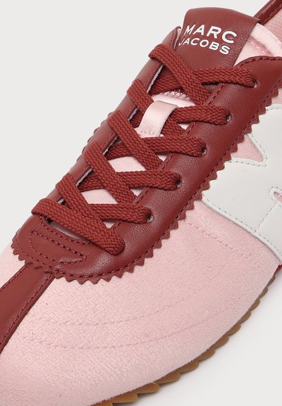 Gros plan d’une basket rose et bordeaux avec des lacets rouges, un accent blanc sur le côté et le logo "MARC JACOBS" sur la languette.