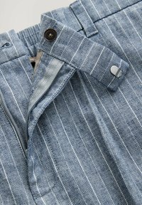 Gestreifte Stoffshorts in Blau und Weiß mit einem Knopfverschluss, ausgestattet mit einem Reißverschluss vorne und einem verstellbaren Bund. Strukturiertes Gewebe-Muster.