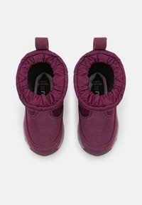 Bottes violettes avec un extérieur en tissu doux, des poignets élastiques et une doublure en peluche. Conception à bout rond avec des semelles texturées pour plus d'adhérence et de stabilité.