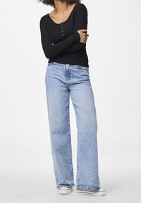 Svart randig långärmad topp med knappar, parat med ljusblå vida jeans och vita sneakers, med en avslappnad passform.