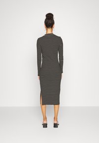 Abito midi a maniche lunghe a righe bianche e nere con spacco laterale, silhouette aderente, materiale elasticizzato, abbinato a sandali con tacco a blocco larghi.