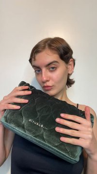 Grønn kosmetikkveske i fløyel med quiltet tekstur og brodert "RITUALS"-logo. Rektangulær form, holdt i hendene, med glatt overflate.