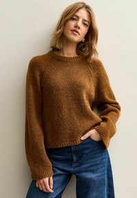 Suéter marrón texturizado con cuello redondo, puños acanalados y dobladillo recortado. Combinado con vaqueros azul oscuro, sobre un fondo claro.