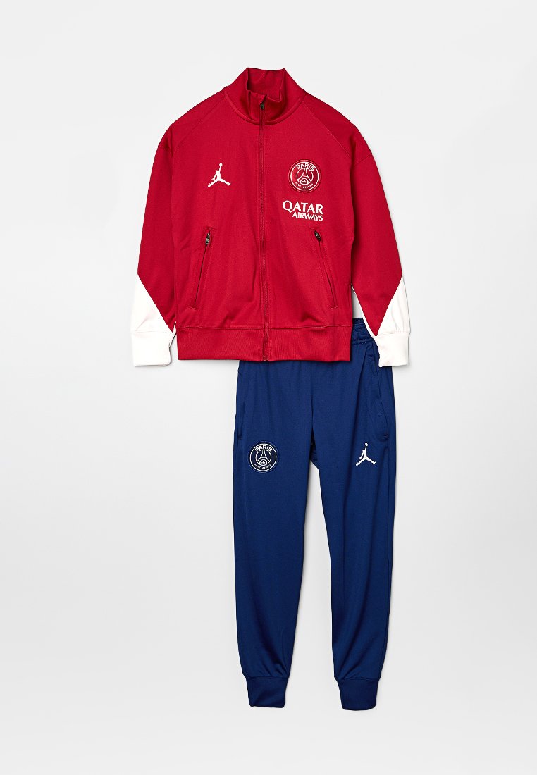 Veste zippée rouge avec accents blancs, logo "Paris" et deux poches zippées ; associée à un pantalon de jogging bleu avec logo et poches latérales.