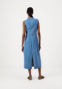 Vestido de mezclilla sin mangas, azul claro, corte recto con cremallera en la espalda y una abertura central. Combinado con zapatos planos de estampado de leopardo.