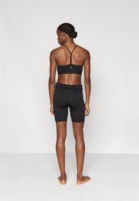 Μαύρο εφαρμοστό αθλητικό σουτιέν με λεπτές τιράντες και μαύρο ψηλόμεσο σορτς, κατασκευασμένα από ελαστικό υλικό, με μικρή λεπτομέρεια λογότυπου στο πίσω μέρος.