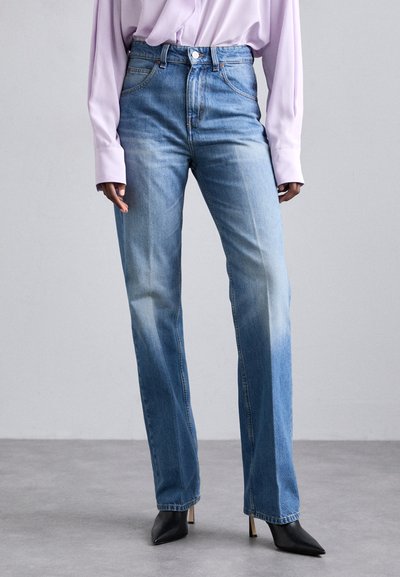 Jean en denim bleu taille haute avec une finition délavée, design à jambe droite et style à cinq poches, associés à des escarpins noirs à bout pointu.