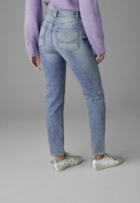 Vaaleansiniset slim fit -farkut, joissa on takataskut ja hienovarainen haalistuminen. Yhdistetty hopeisiin kenkiin ja violettiin neuleeseen.