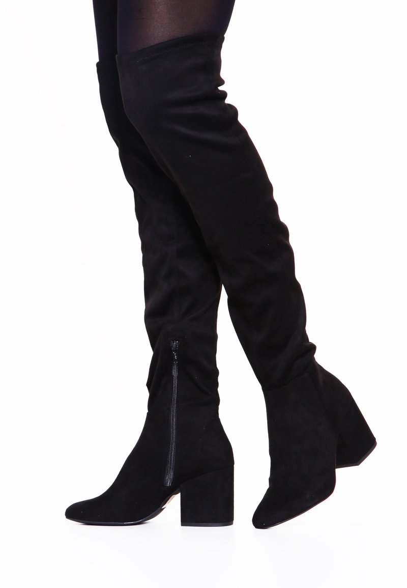 Černé kozačky nad kolena vyrobené z měkké semišové kůže s špičatou špičkou, boční zipovou uzávěrkou a robustním podpatkem pro dodatečnou stabilitu.