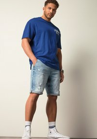 Blauwe katoenen T-shirt met grafische details, gecombineerd met lichtblauwe denim shorts met rafelige randen. Witte high-top sneakers maken de look af.