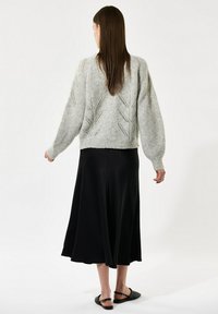 Grå strikket sweater med en løs pasform, præget af et bladmønster og ribbet kant. Kombineret med en sort svajende nederdel og flade sandaler.