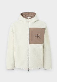 Casaco de fleece com fecho em off-white com um bolso castanho. Apresenta capuz, tecido texturizado e o logótipo "Calvin Klein" no bolso.